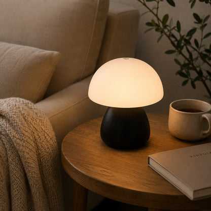 Lampe champignon Petite Nocturne noire allumée sur une table en bois dans un coin cosy