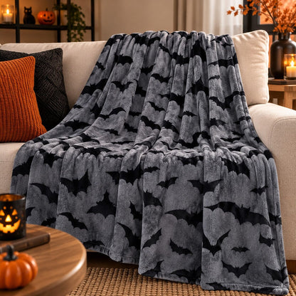 Plaid Halloween gris à motifs chauves-souris noires installé sur un canapé dans un salon chaleureux aux accents d’automne